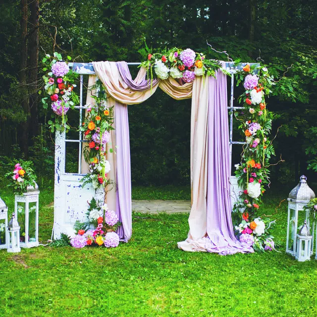 A wedding arch with flowers and candles in the grass.